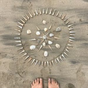 Footsteps lead to a creative seashell mandala on a sandy beach, embodying tranquility.